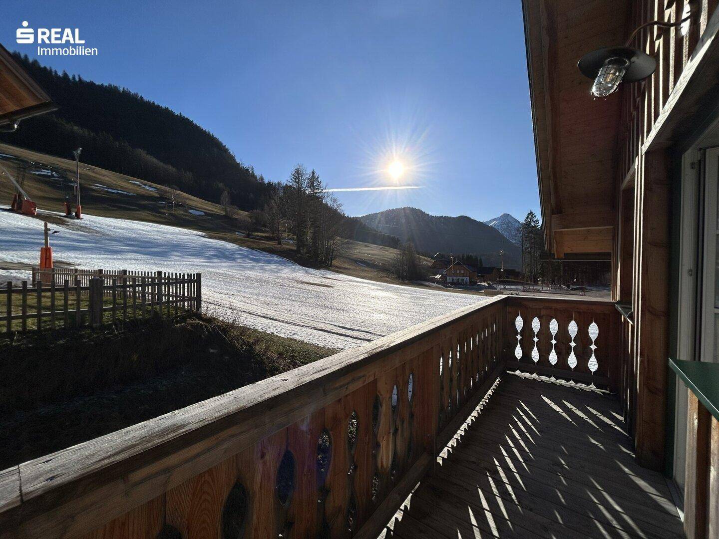Sonniger Balkon mit Holzbalkonbrüstung und Blick auf die verschneite Berglandschaft.