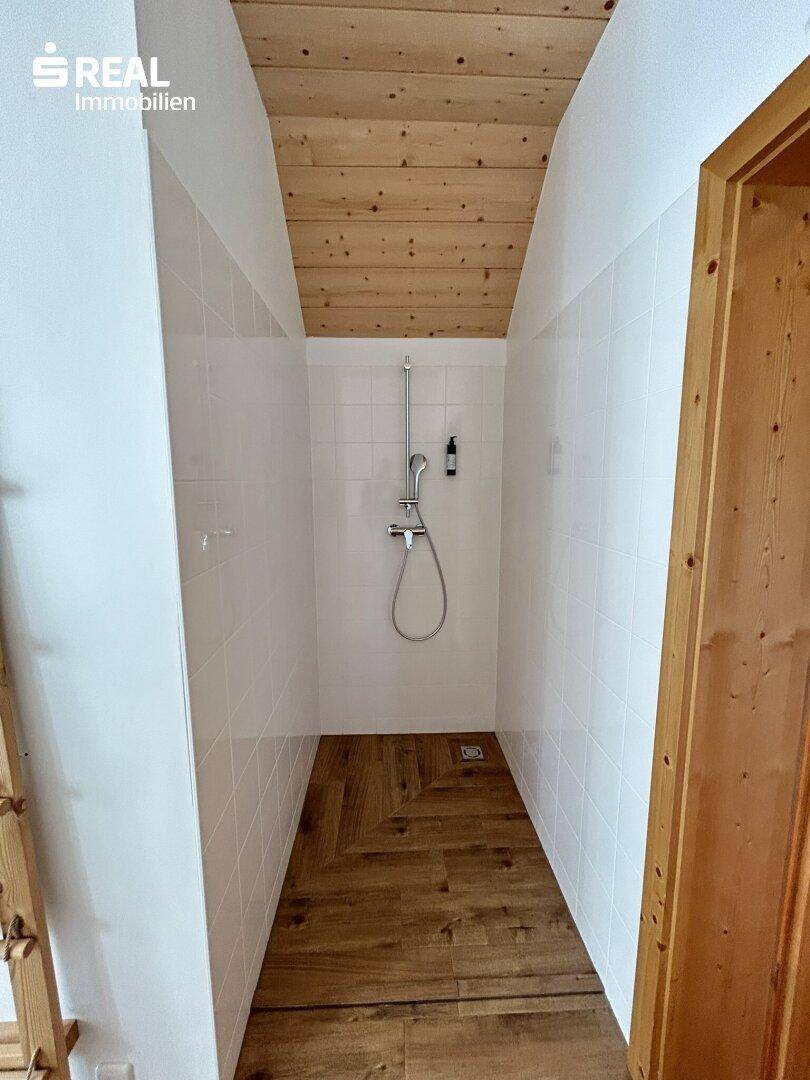 Moderne Duschkabine mit weißen Fliesen und Holzboden im Badezimmer.