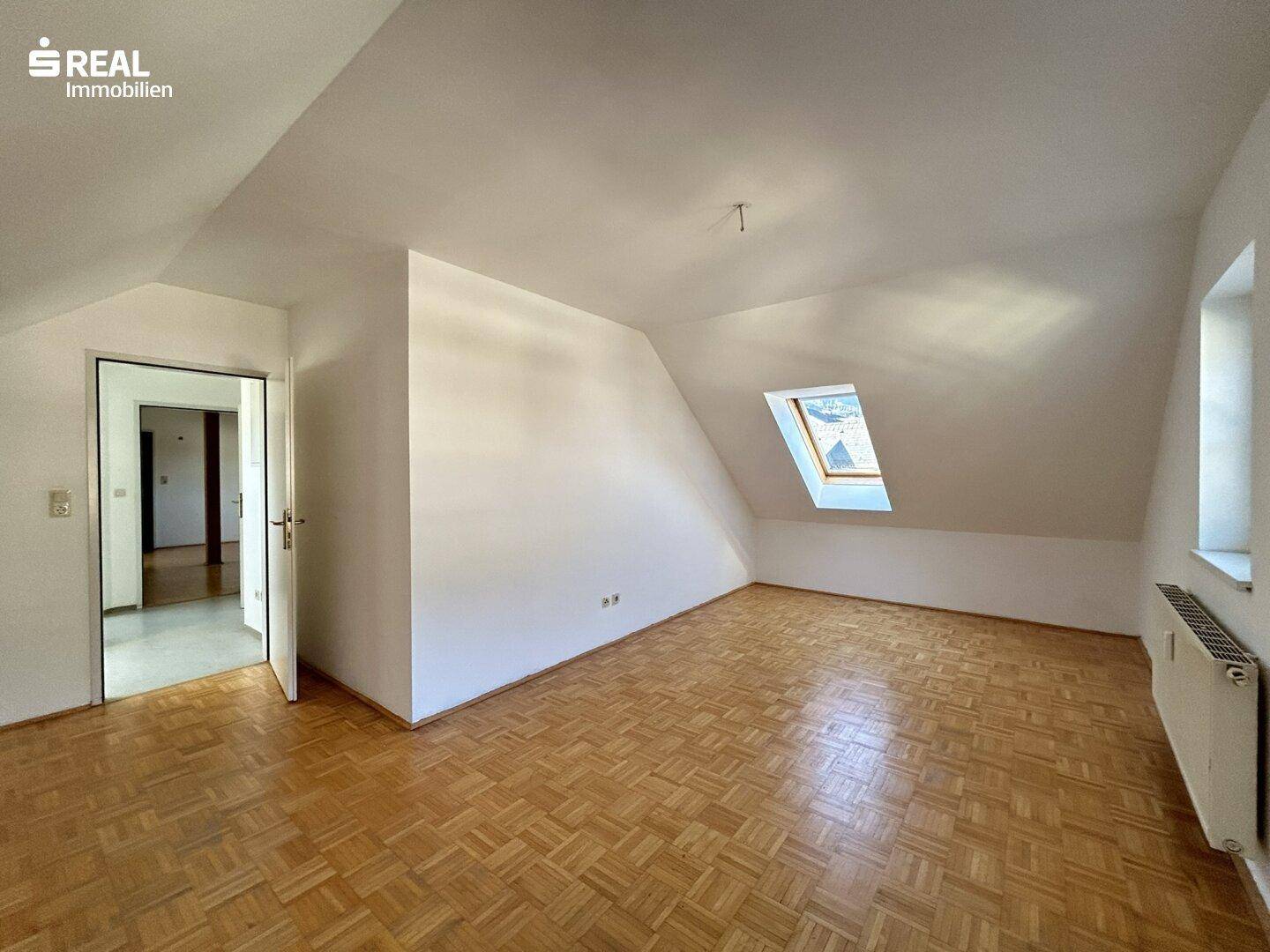 Geräumiges Wohnzimmer im Dachgeschoss mit Parkettboden und schrägen Wänden.