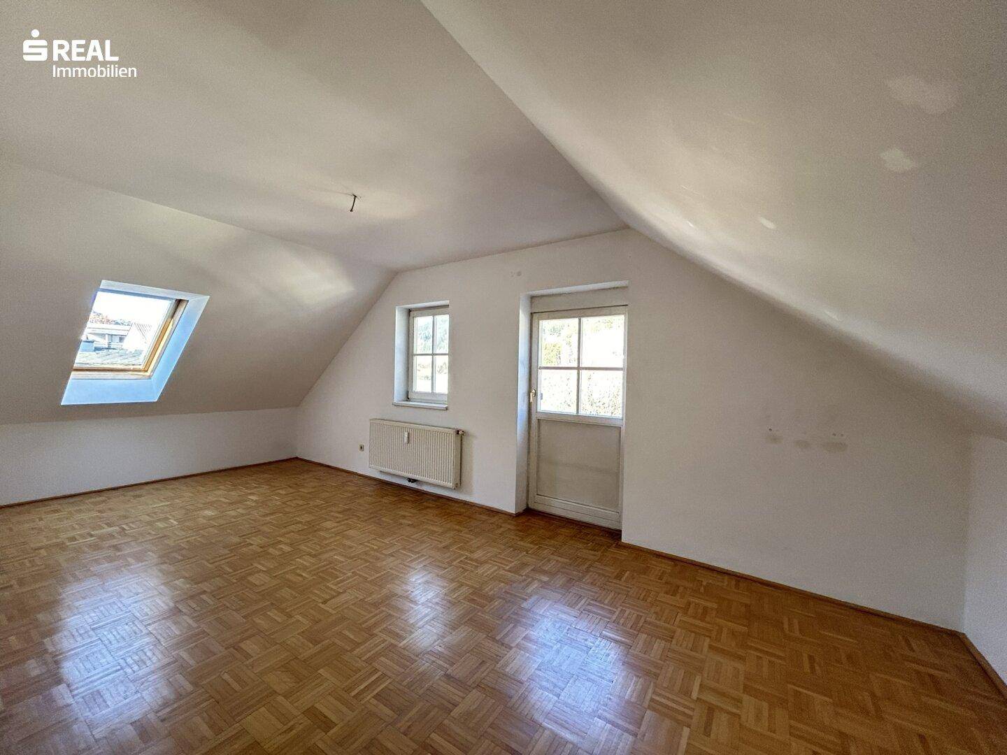 Lichtdurchflutetes Wohnzimmer mit Parkettboden, Dachfenster und Zugangstür.
