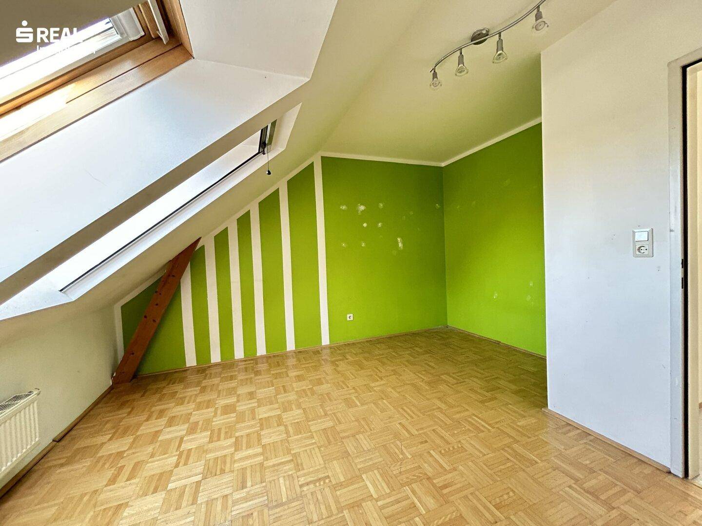 Schlafzimmer mit Parkettboden, grüner Akzentwand und Dachfenster.