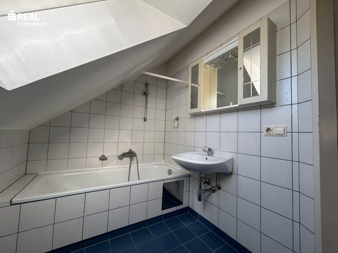 Badezimmer mit Badewanne, Waschbecken und weißen Fliesen unter einem Dachfenster.
