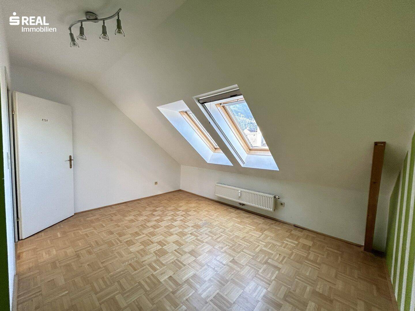 Helles Schlafzimmer mit Parkettboden und zwei Dachfenstern für viel Tageslicht.