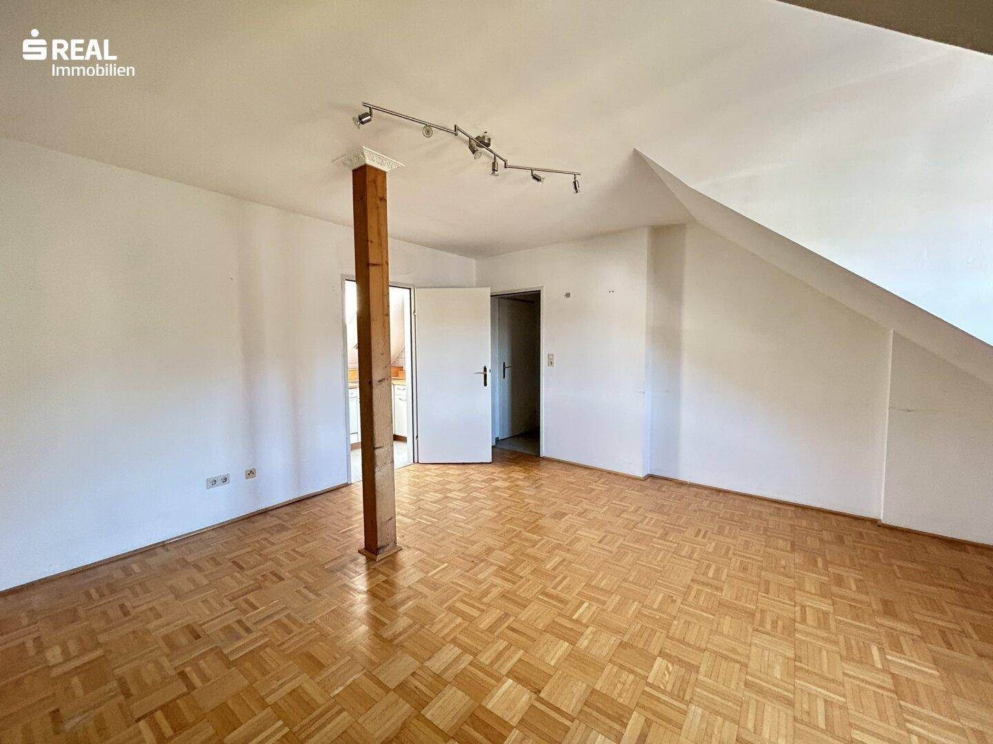 Großes Wohnzimmer mit Parkettboden, Holzbalken und Zugang zu weiteren Räumen.