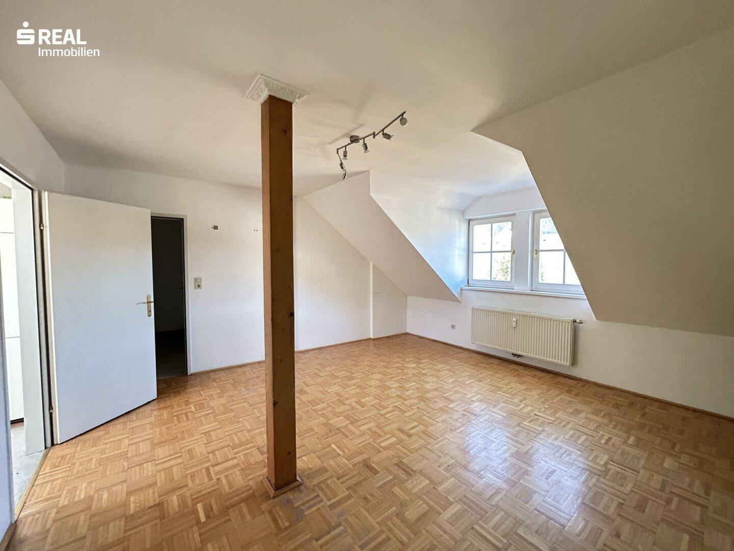Geräumiges Wohnzimmer mit Holzbalken, Parkettboden und Fenstern.