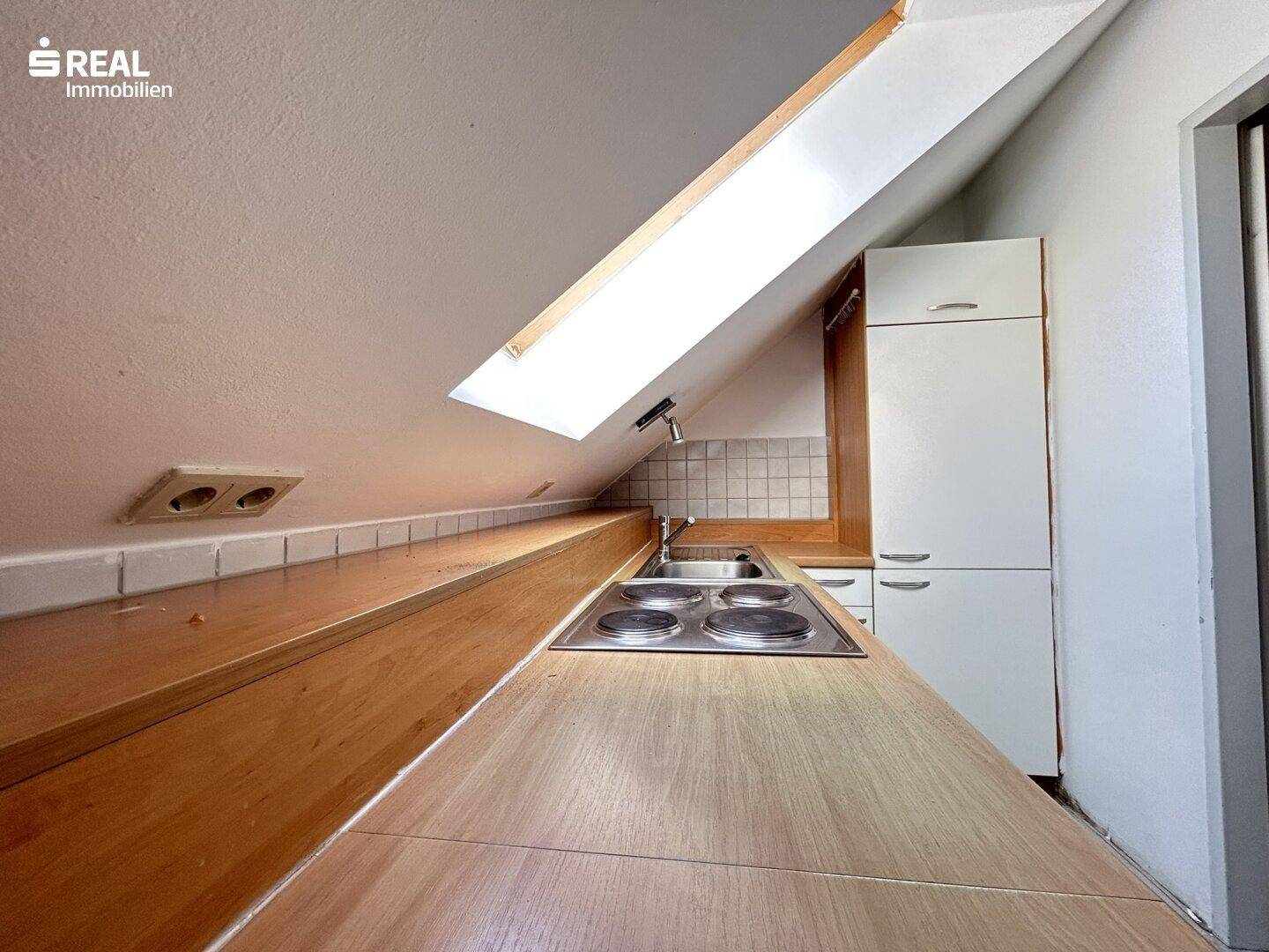 Küchenzeile mit Holz-Arbeitsplatte und integriertem Kochfeld unter einem großen Dachfenster.
