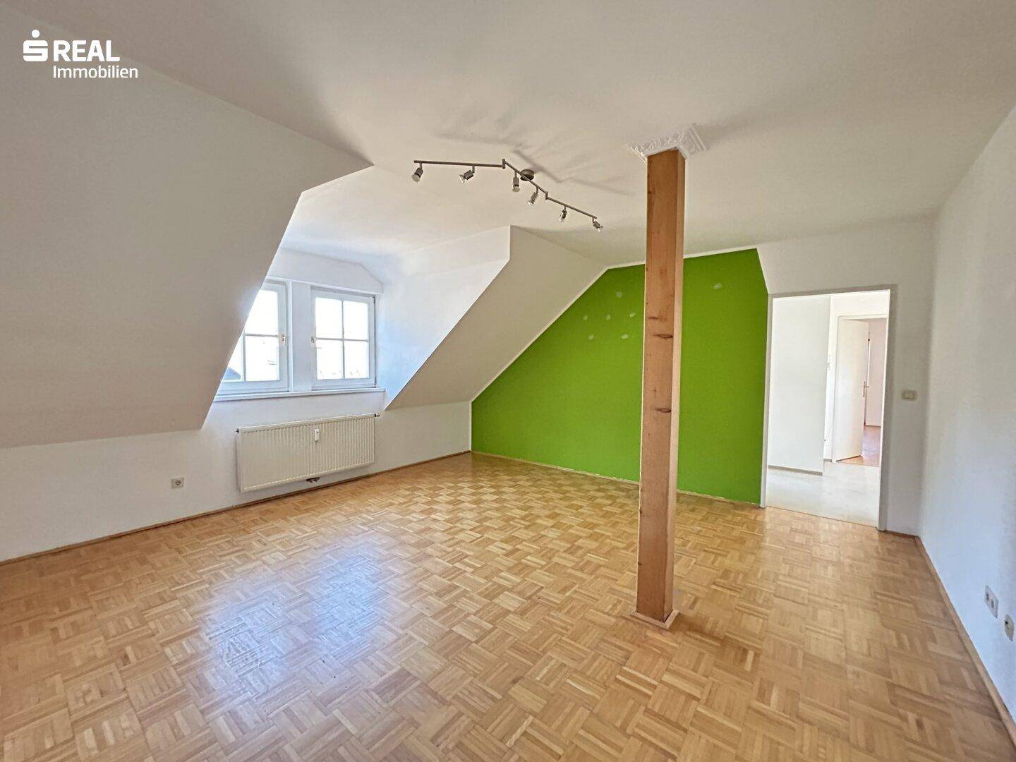 Helles Wohnzimmer mit Parkettboden, Holzbalken und grüner Akzentwand.