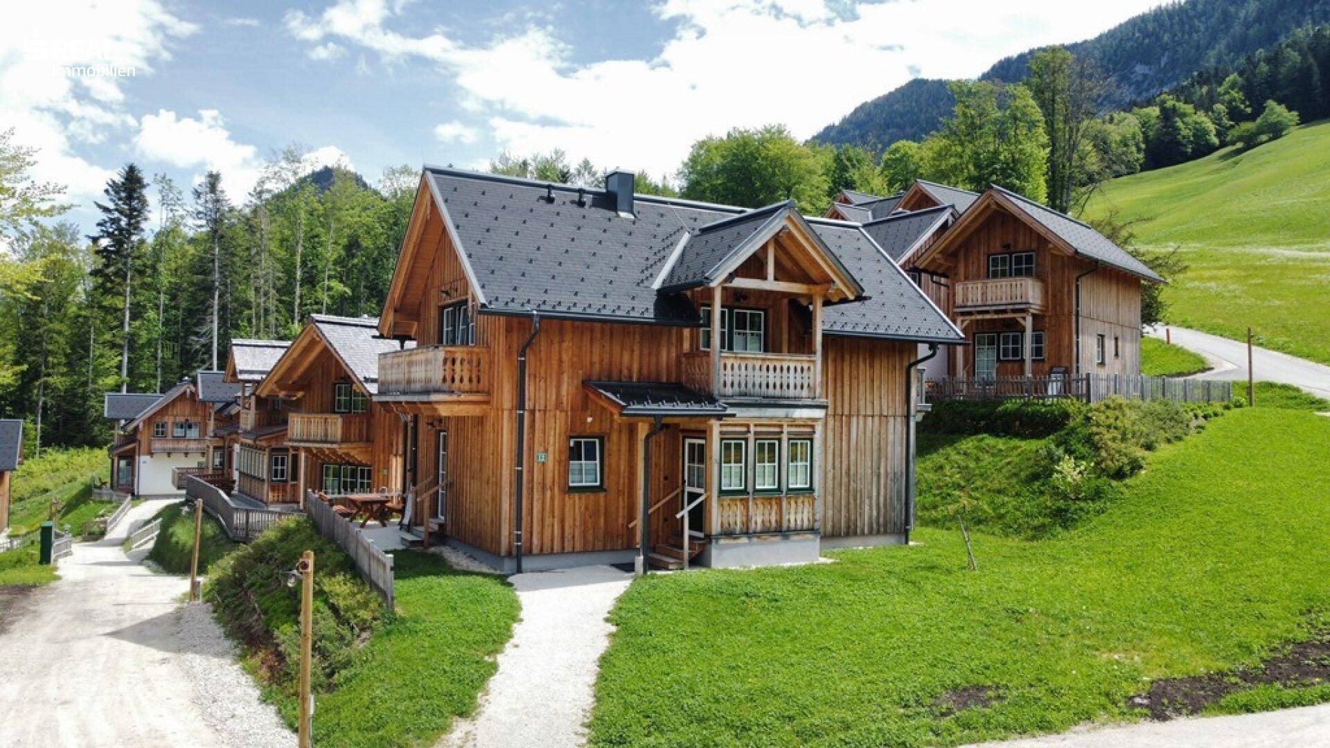 Mehrere Holzhäuser im alpinen Stil in einer malerischen Berglandschaft unter blauem Himmel.