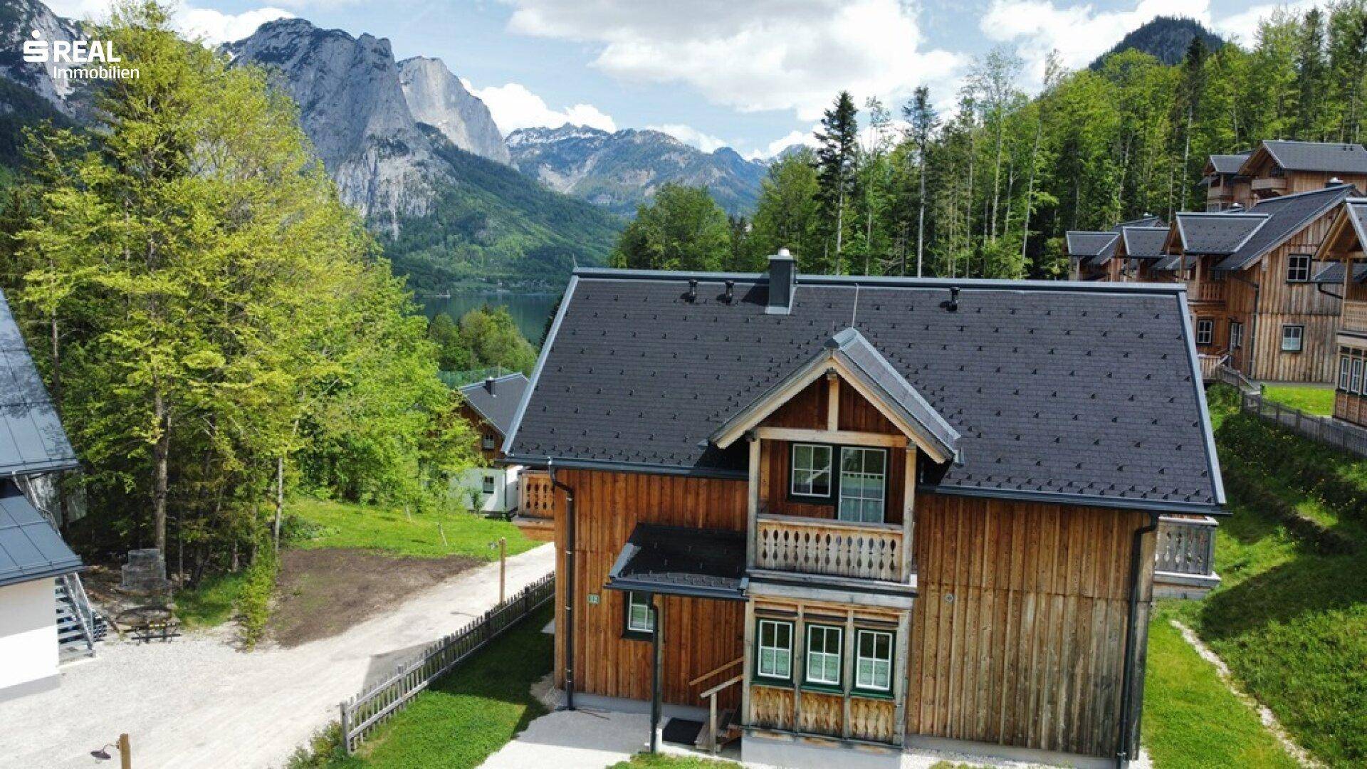 Vogelperspektive eines Holzhauses mit Blick auf einen See und die umliegende Berglandschaft.