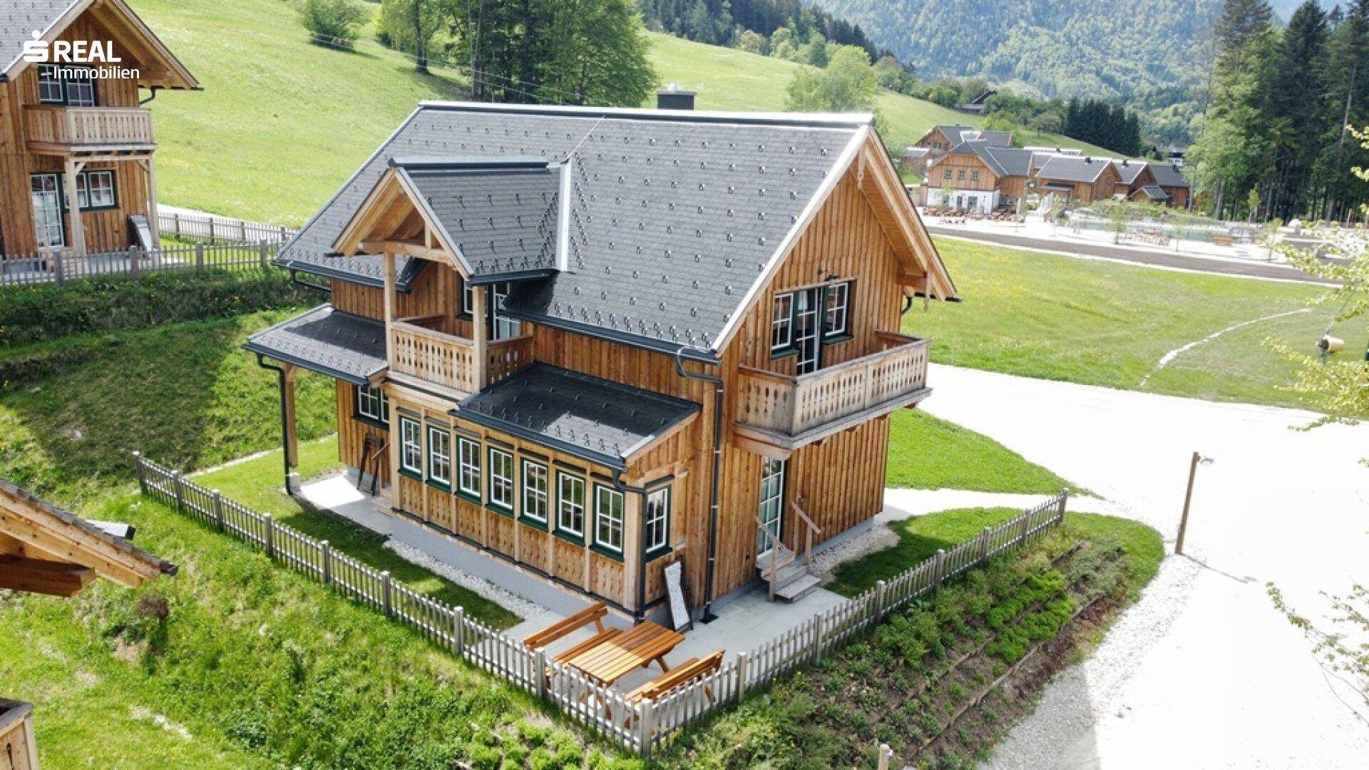 Holzhaus im alpinen Stil mit kleinem Gartenbereich und Holztischgarnitur, umgeben von grünen Hügeln.