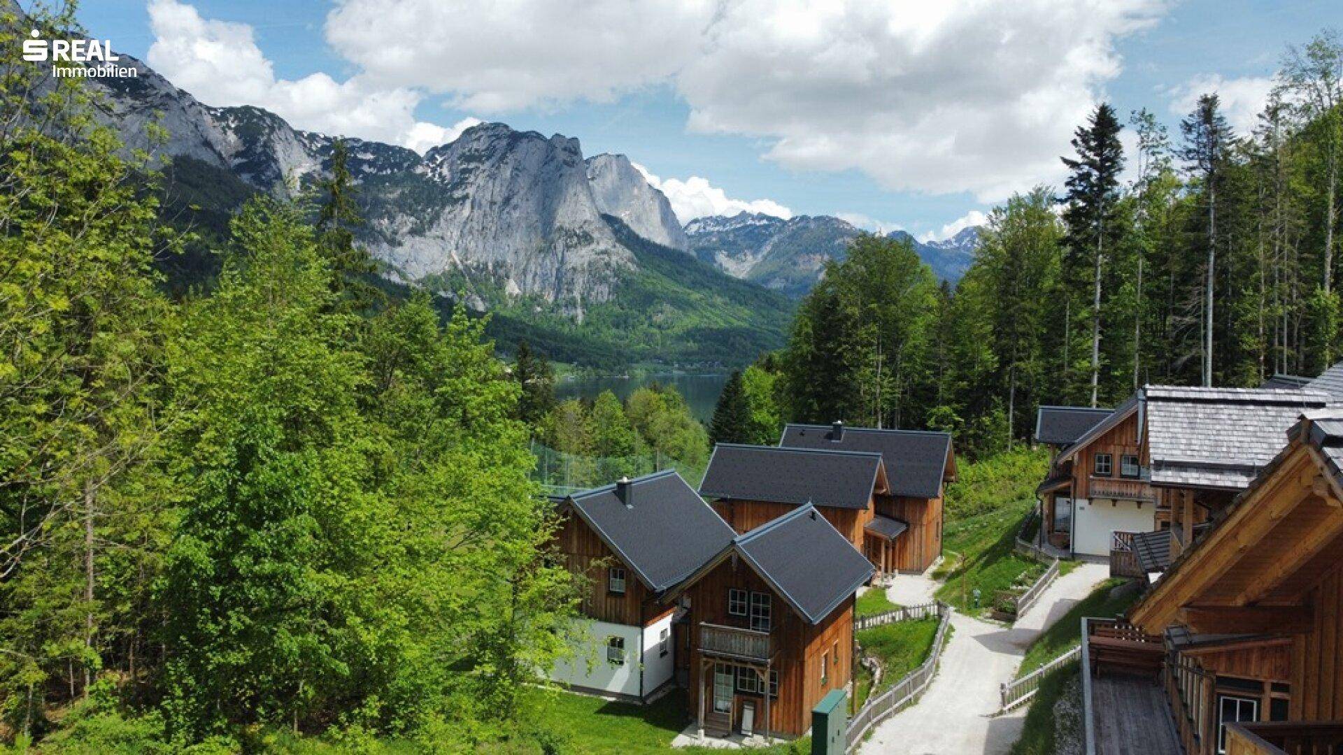 Luftaufnahme einer Siedlung von Holzhäusern mit Blick auf einen malerischen See und die majestätischen Berge.