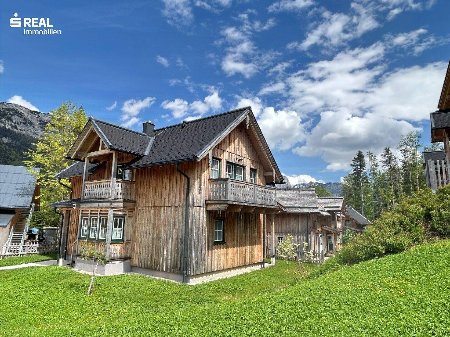 Charmantes Holzhaus mit traditionellen Balkonen und grünen Fensterrahmen, eingebettet in eine idyllische Bergkulisse.