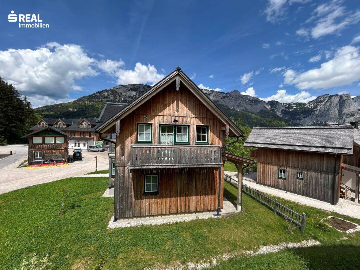 Vorderansicht eines Holzhauses mit Balkonen und grünen Fensterrahmen, vor einer beeindruckenden Bergkulisse.