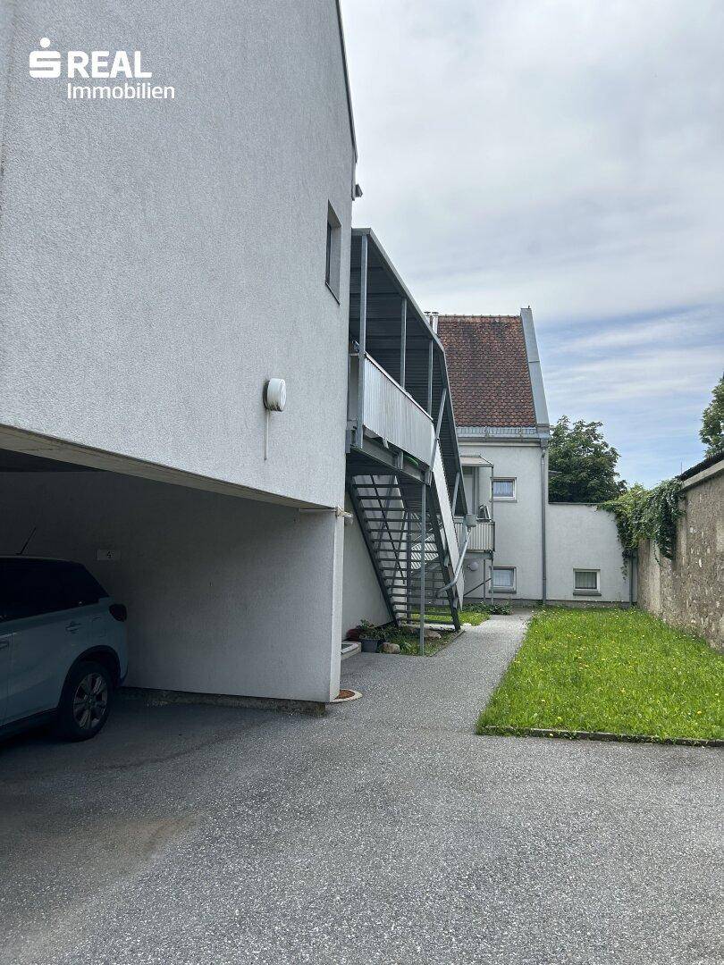 Seitenansicht eines Gebäudes mit einem überdachten Parkplatz und einer Außentreppe, die zu den oberen Etagen führt.
