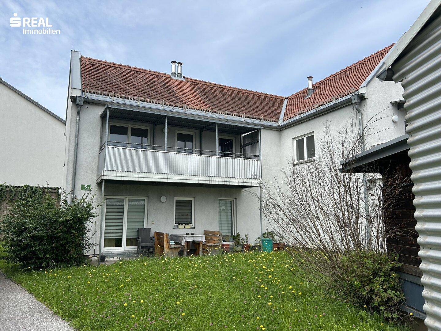 Rückseite eines Wohngebäudes mit einer kleinen Terrasse im Erdgeschoss und einem Balkon im Obergeschoss.
