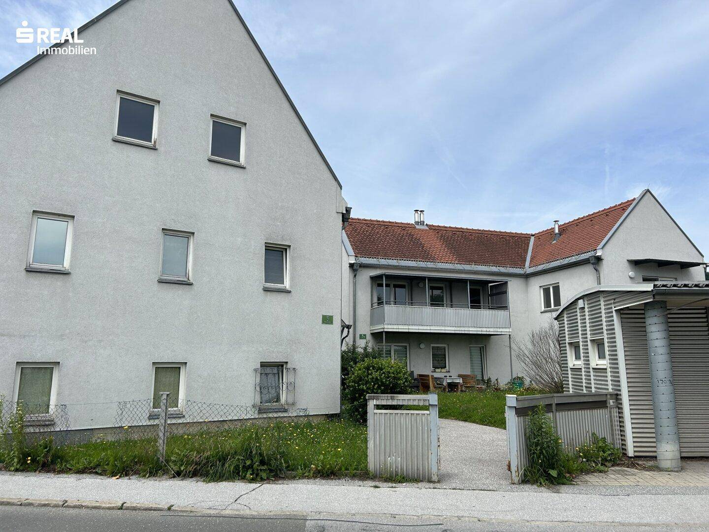 Ansicht eines Wohnkomplexes mit mehreren Gebäuden, einem gepflasterten Weg und einem kleinen Gartenbereich.