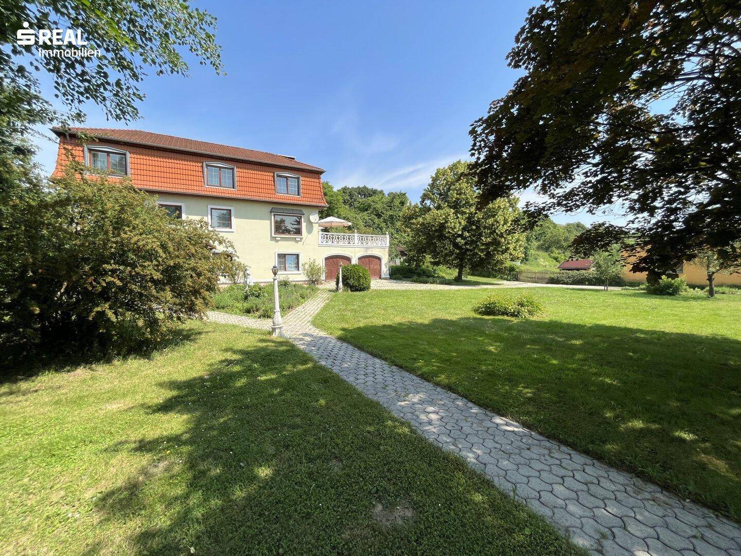 Hausansicht von der Gartenseite mit gepflastertem Weg und weitläufiger Rasenfläche.
