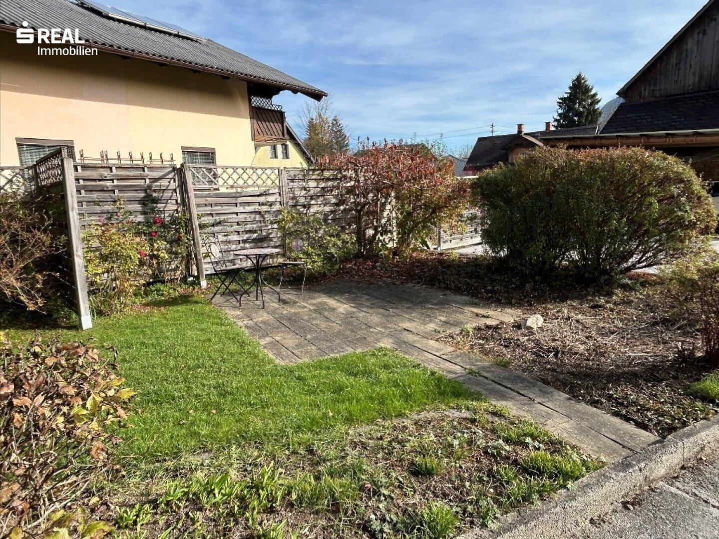 Kleiner gepflasterter Terrassenbereich mit Holzzaun und Sitzgelegenheit im Garten.