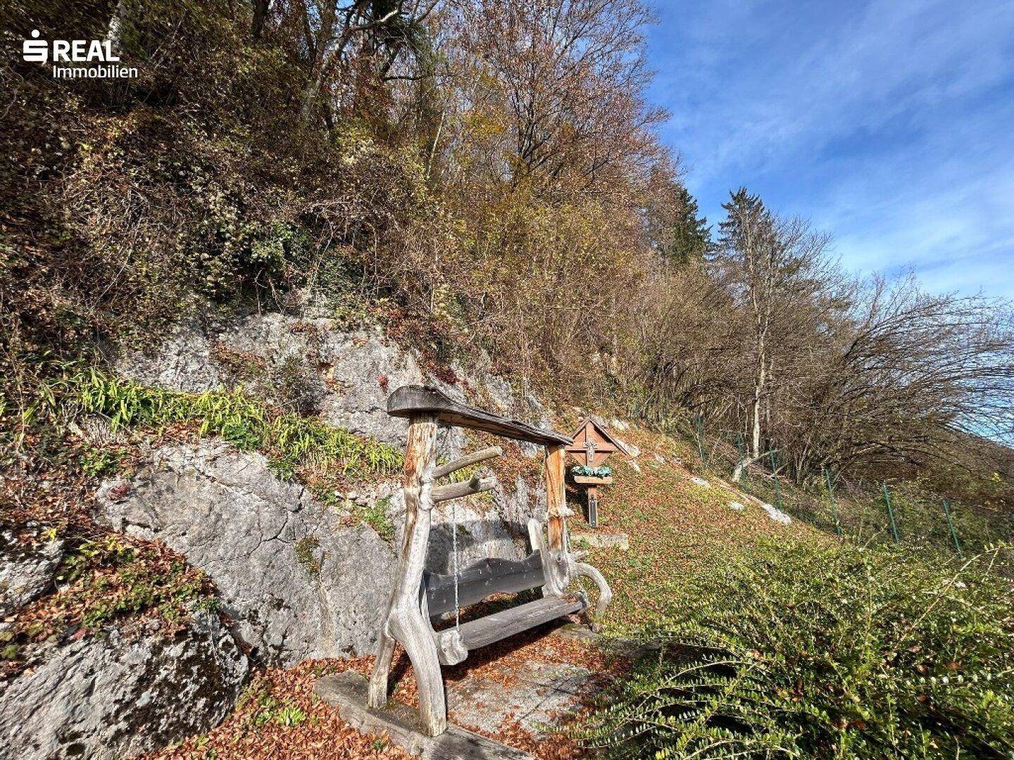 Rustikale Holzschaukelbank am felsigen Hang, umgeben von herbstlicher Vegetation.