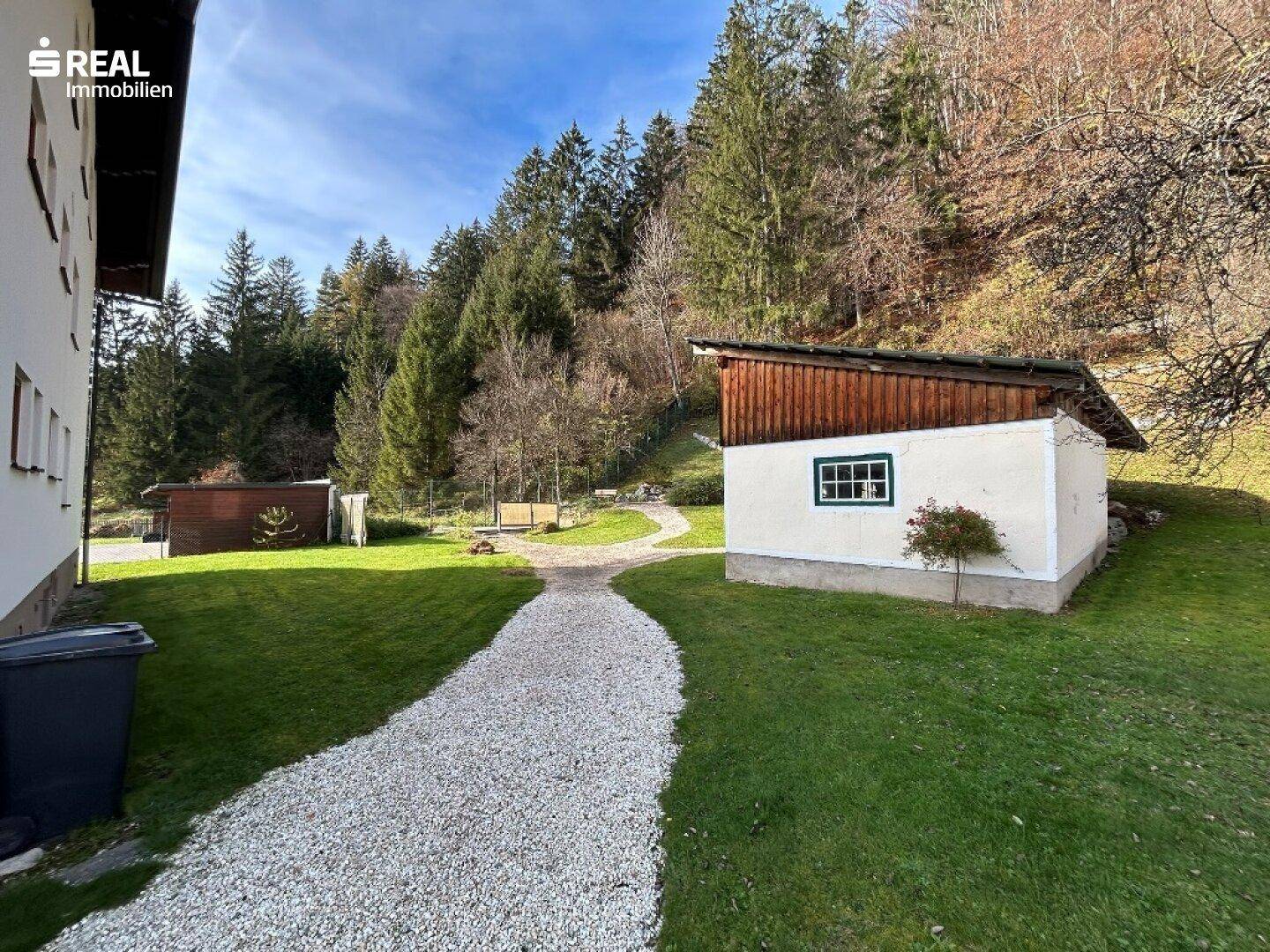 Kiesweg führt zu einem Nebengebäude, umgeben von grünen Wiesen und Bäumen.
