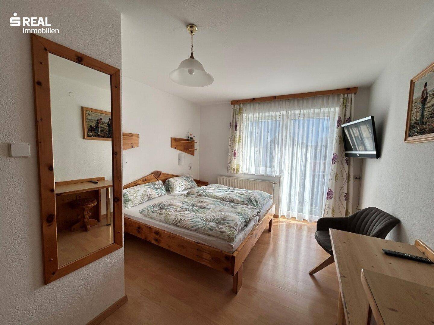 Helles Schlafzimmer mit Doppelbett, Holzmöbeln und Zugang zu einem Balkon.