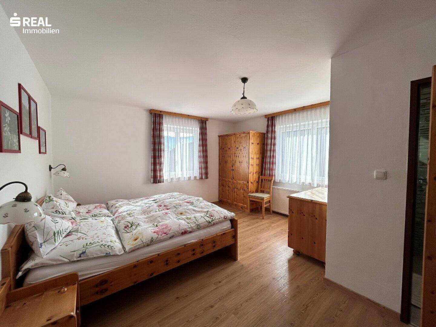 Helles Schlafzimmer mit Doppelbett, Holzschrank und Fenstern für viel Tageslicht.