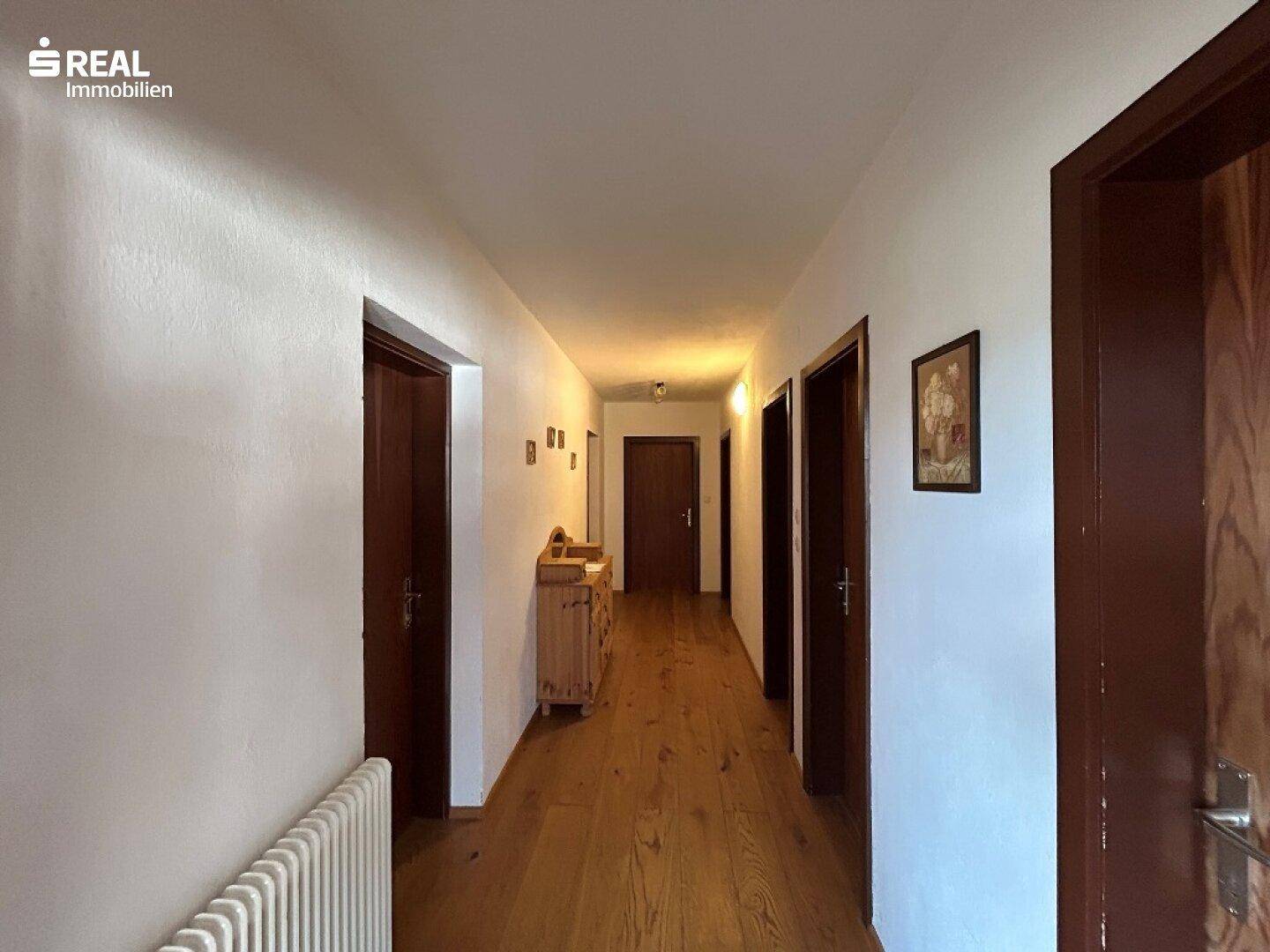 Heller Flur mit Holzfußboden, weißen Wänden und mehreren Holztüren.