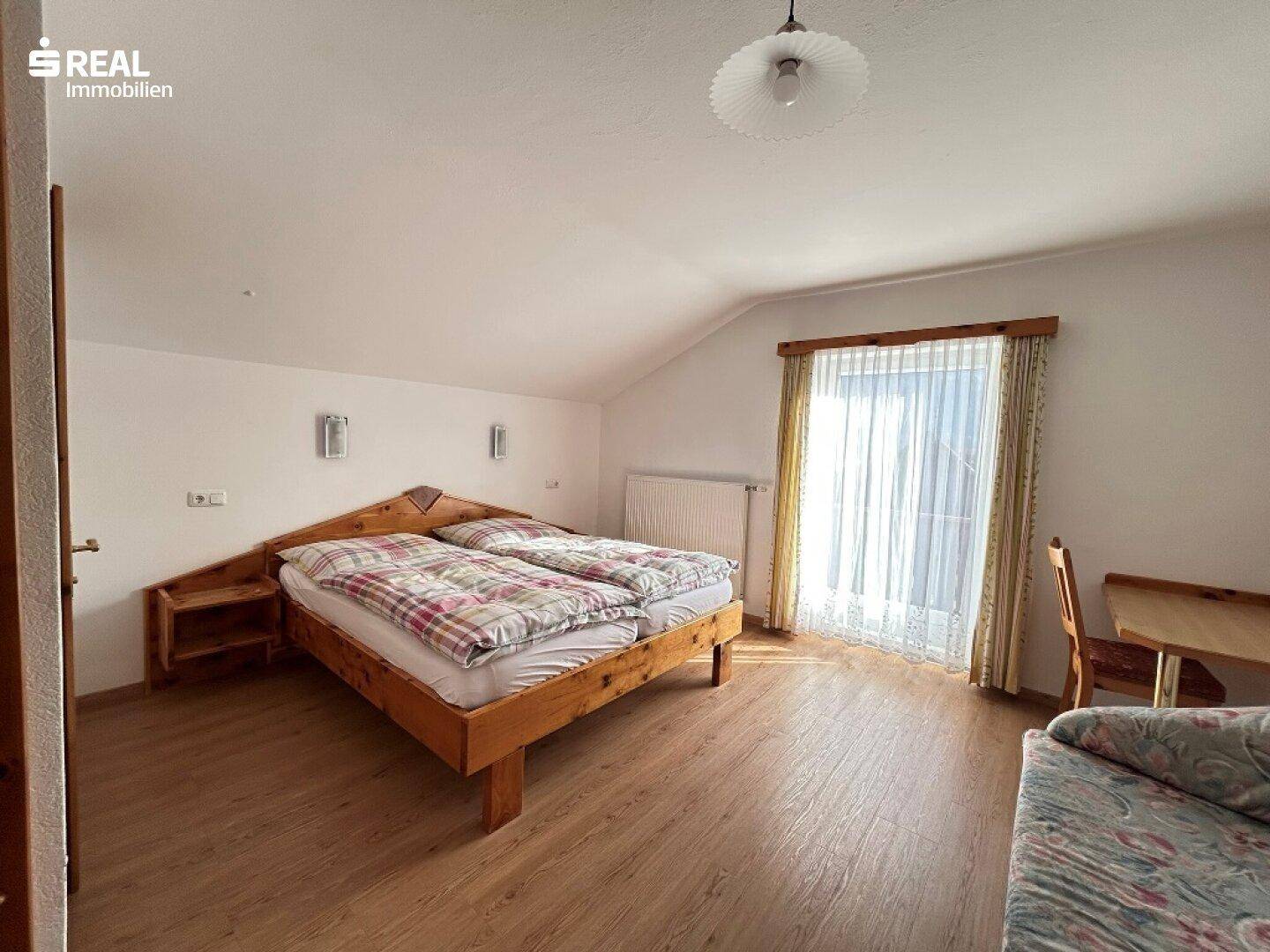 Helles Schlafzimmer mit Dachschräge, Holzfußboden und einem großen Fenster.