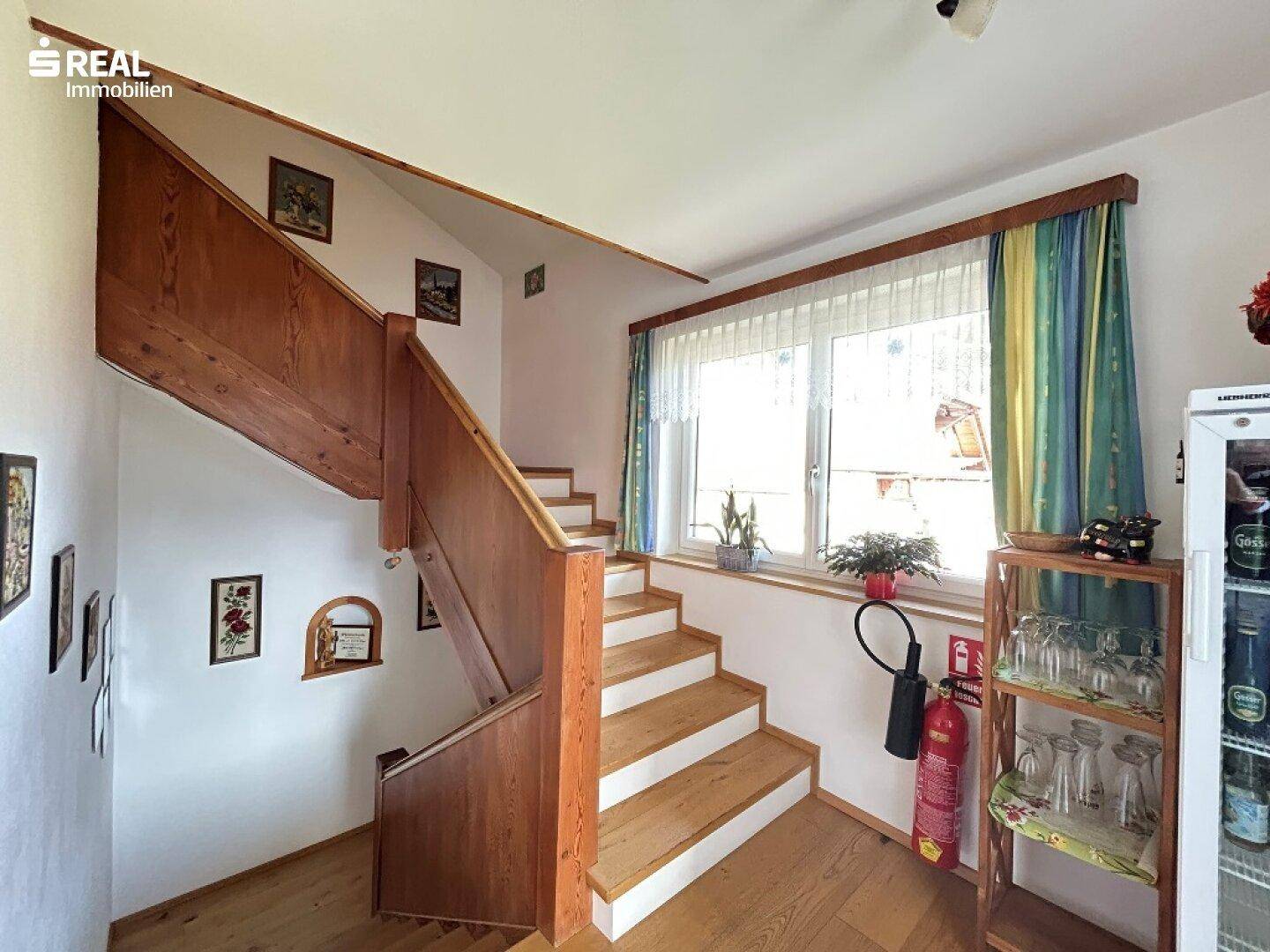 Treppenhaus mit Holztreppe, großem Fenster und kleiner Bar-Ecke.