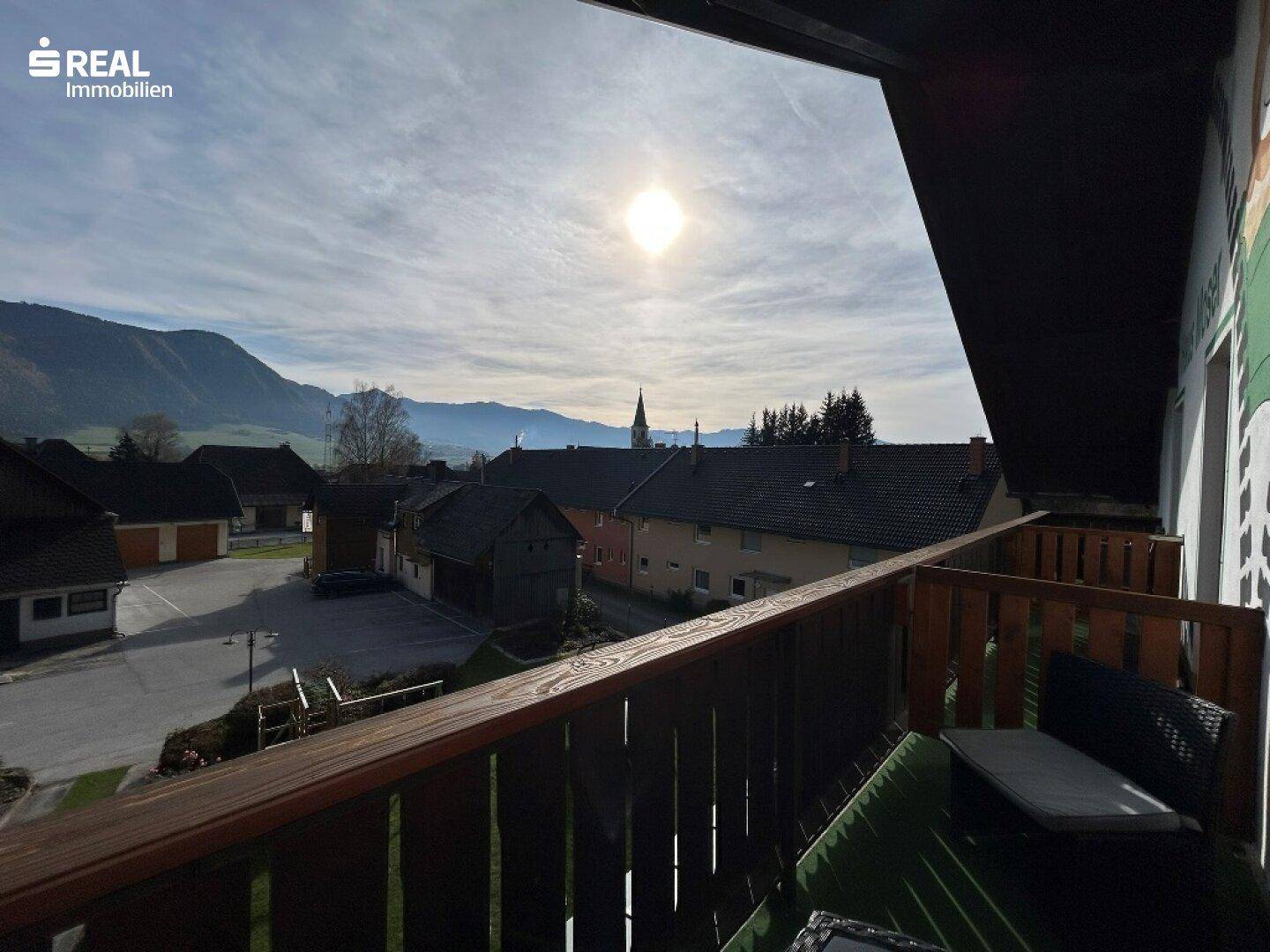 Sonniger Balkon mit Holzbalkonmöbeln und malerischem Blick auf die Berge und das Dorf.