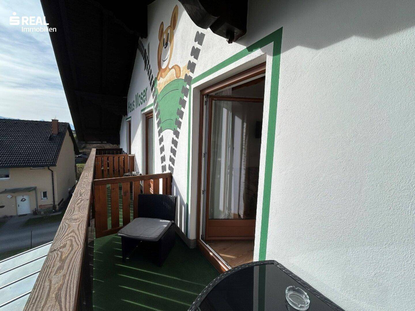 Balkon mit Holzbalkonmöbeln und einer farbenfrohen Wandmalerei an der Fassade.