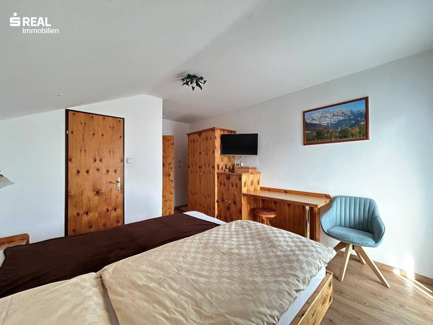 Schlafzimmer mit Holzmöbeln, Fernseher und einem Bild mit Bergblick.