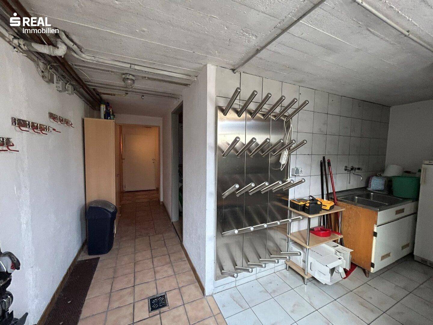 Funktionaler Hauswirtschaftsraum mit Waschbecken, Fliesenboden und praktischem Weinregal an der Wand.