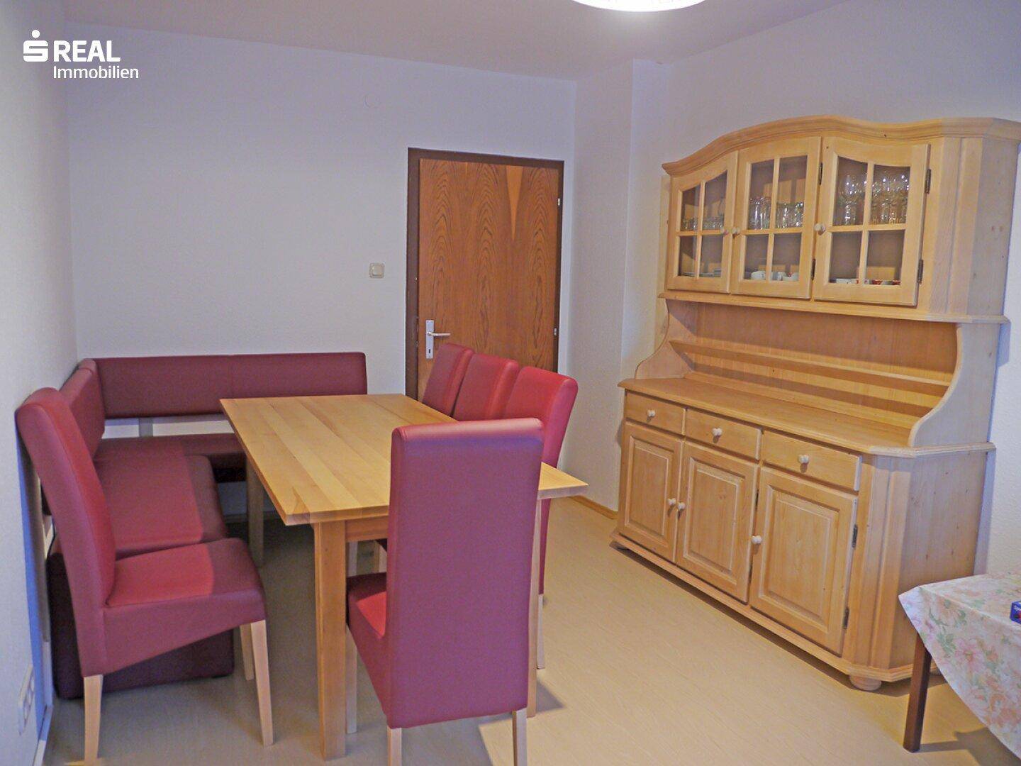 Gemütlicher Essbereich mit Holztisch, roter Sitzbank und einem großen Holzschrank.