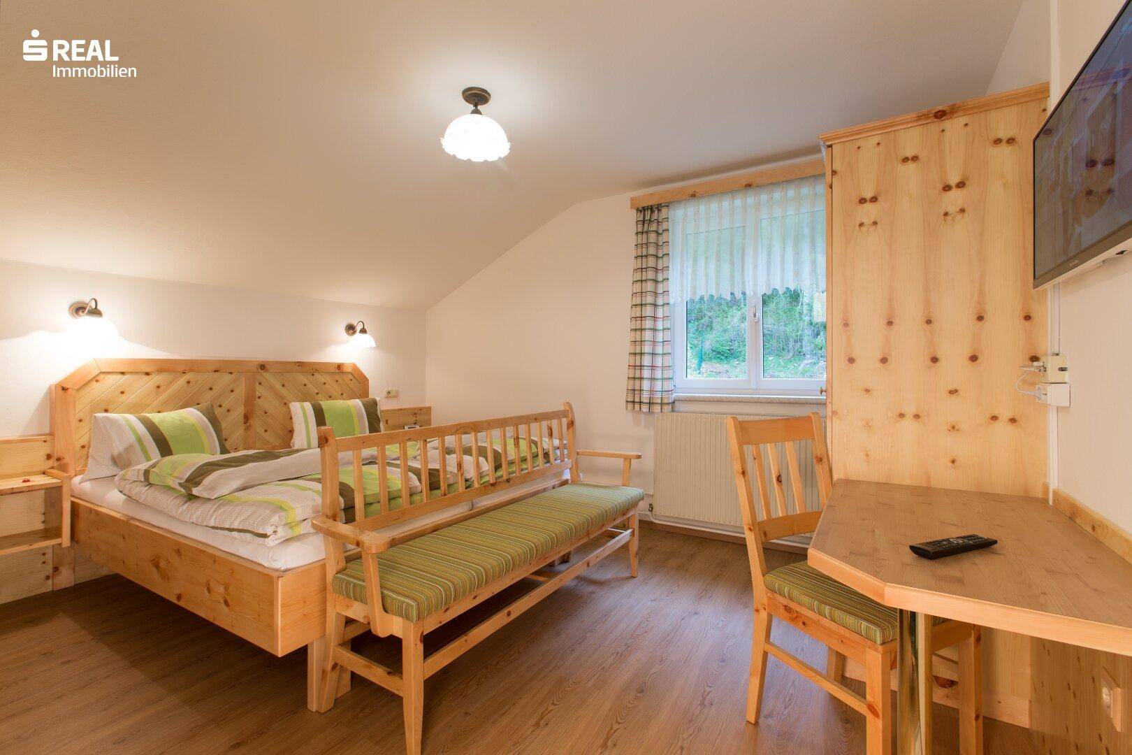 Gemütliches Schlafzimmer mit Dachschräge, Holzmöbeln und Blick ins Grüne.