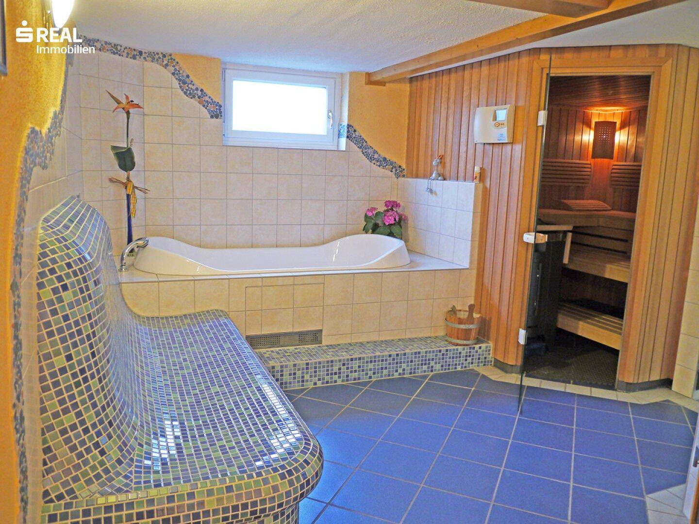 Wellnessbereich mit Sauna, Badewanne, Mosaikbank und blauen Fliesen.