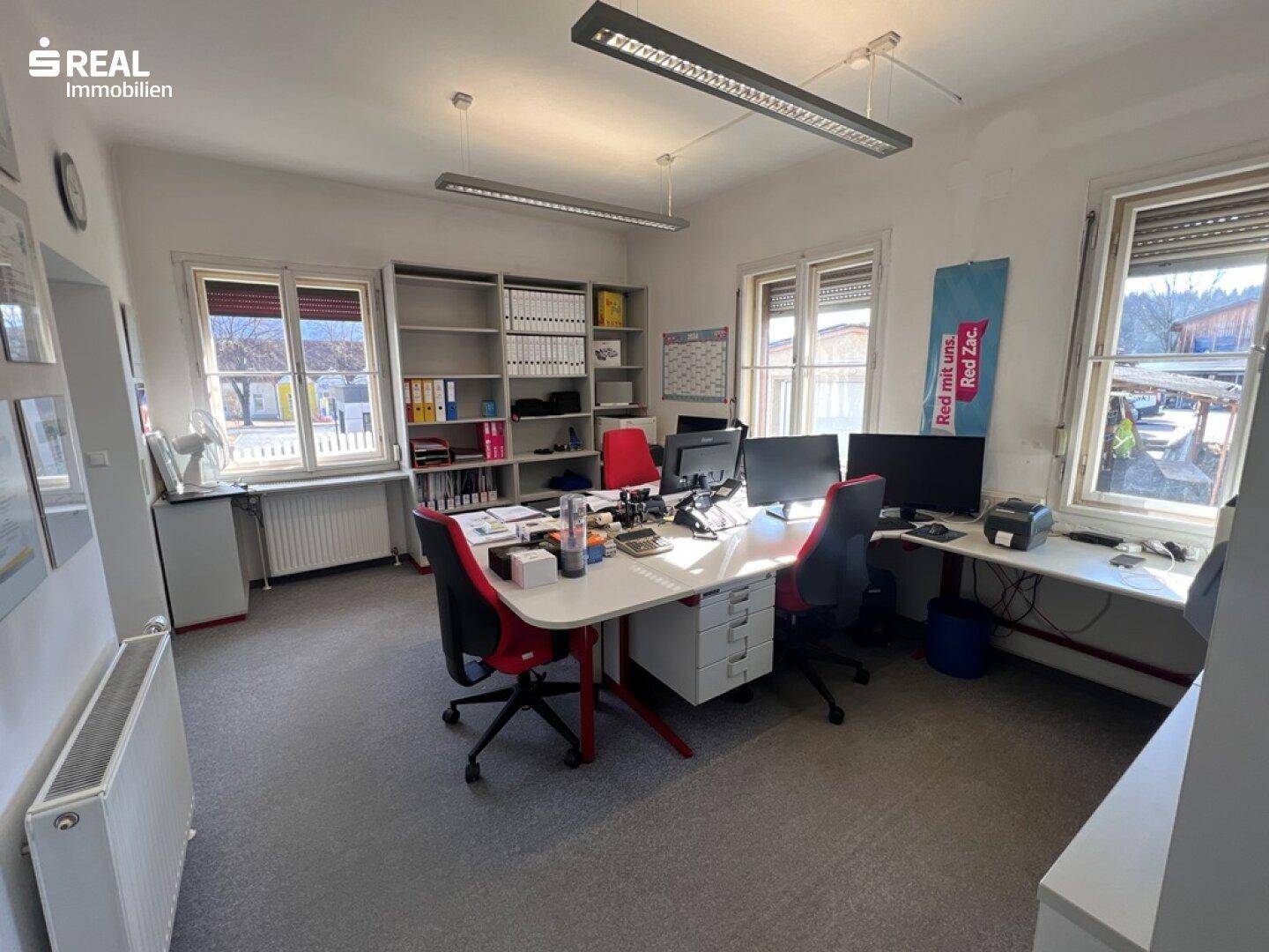 Helles Büro mit mehreren Arbeitsplätzen, großen Fenstern und Blick ins Grüne.