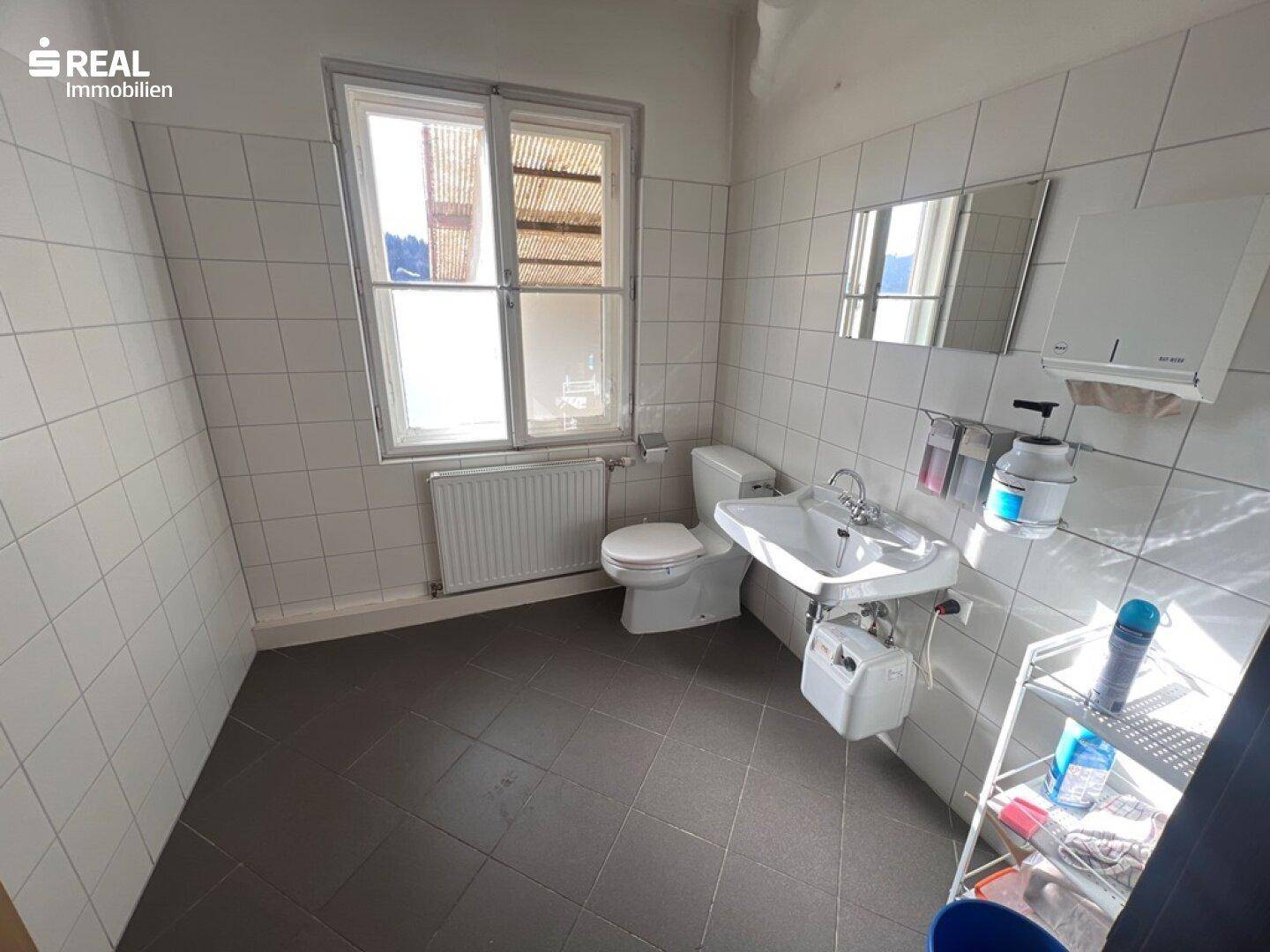 Einfaches WC mit Waschbecken, Toilette und Fenster, hell gefliest.