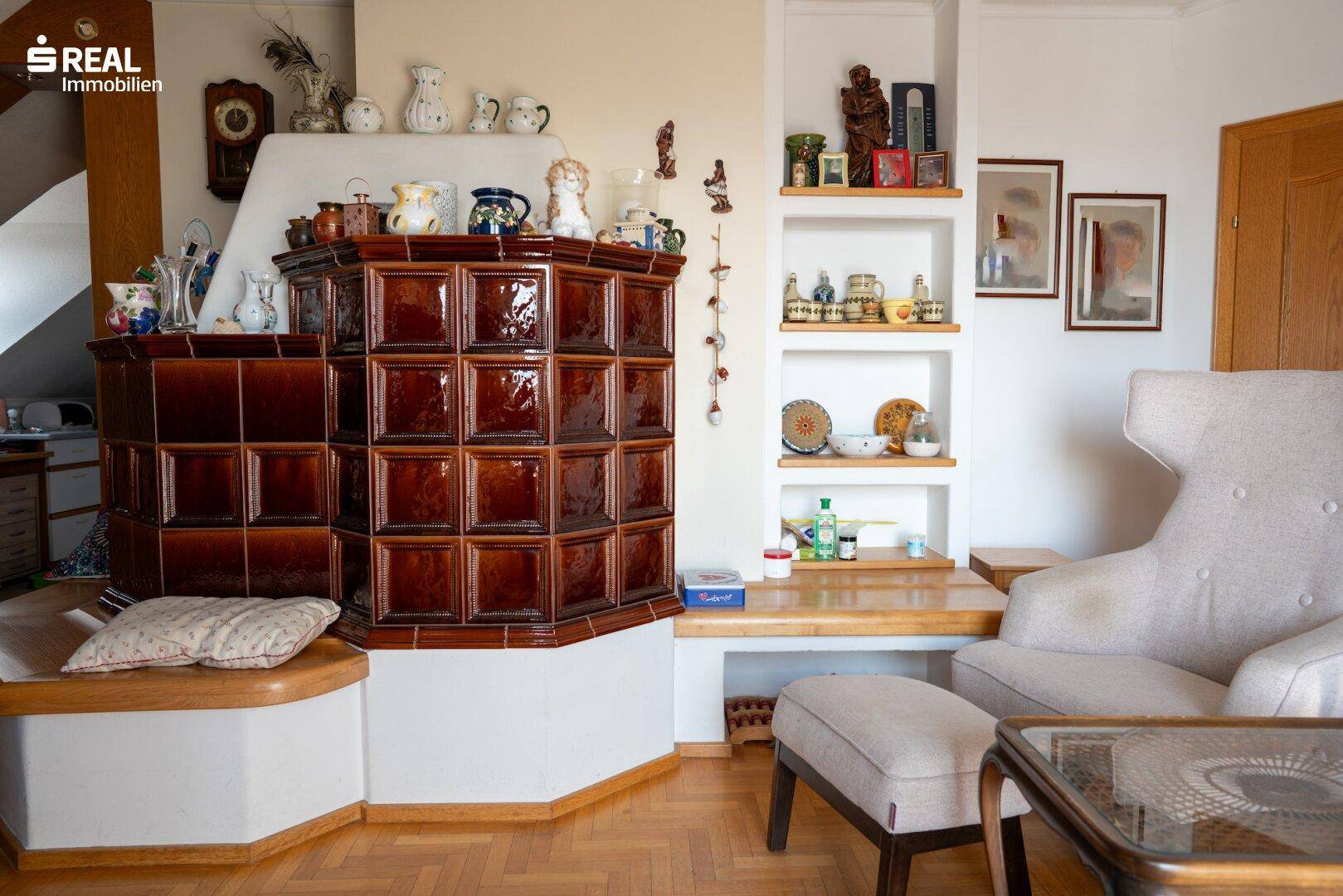 Wohnzimmer mit traditionellem Kachelofen, Holzboden und eingebauten Regalen.