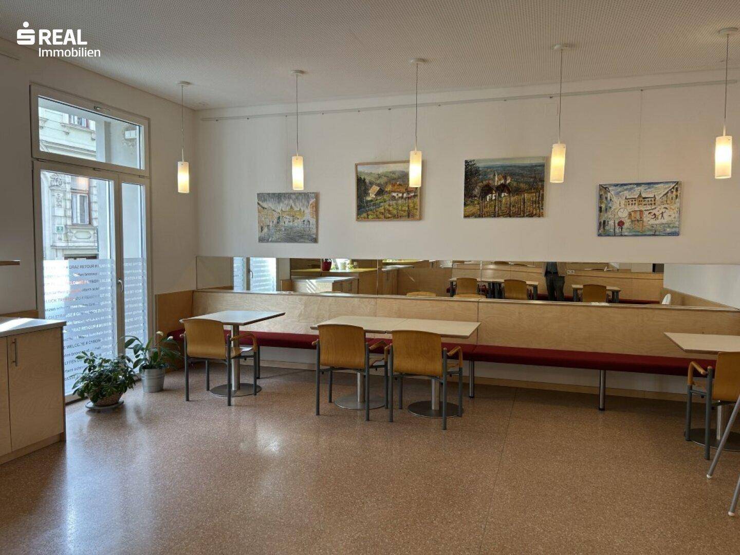Heller Speisesaal mit langen Holzbänken, Tischen und dekorativen Bildern an den Wänden.