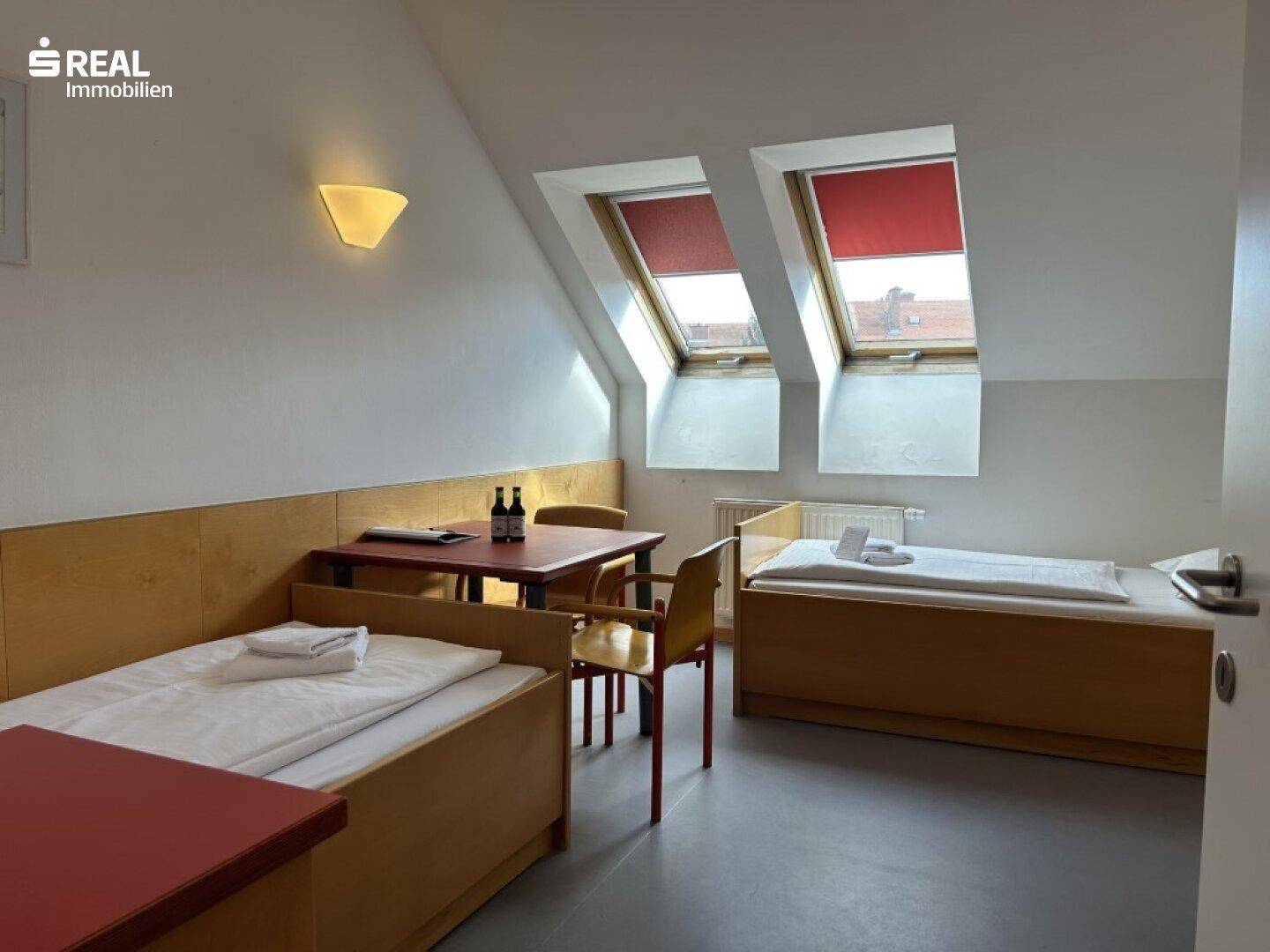 Schlafzimmer im Dachgeschoss mit zwei Einzelbetten, einem Tisch und Dachfenstern.