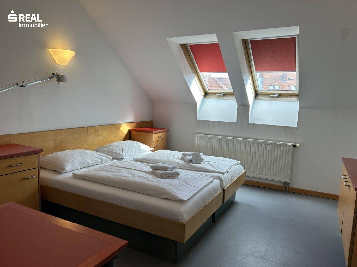 Helles Schlafzimmer im Dachgeschoss mit Doppelbett, Heizung und zwei Dachfenstern.