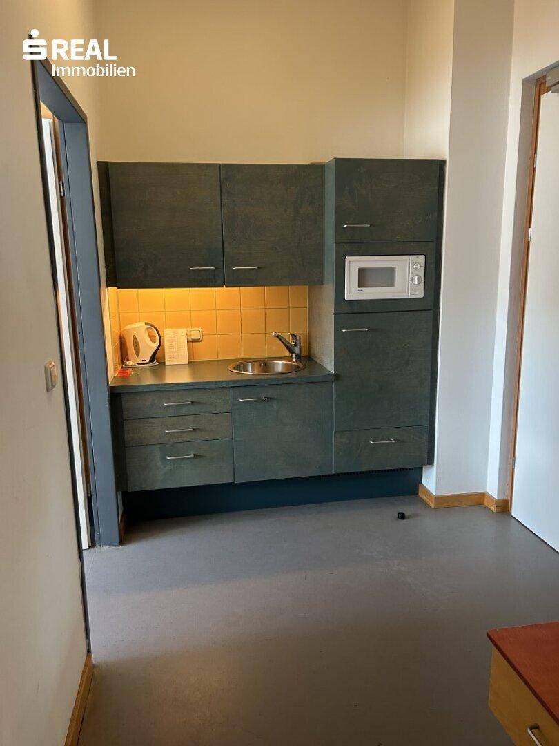 Kleine Küchenzeile mit Spüle, Mikrowelle und dunklen Holzschränken in einem Zimmer.