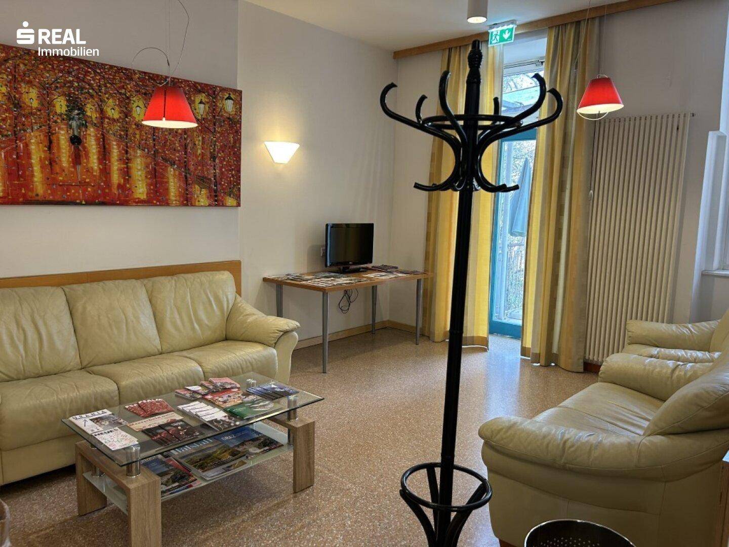 Gemütlicher Wartebereich mit beigen Sofas, Couchtisch und farbenfrohem Wandbild.