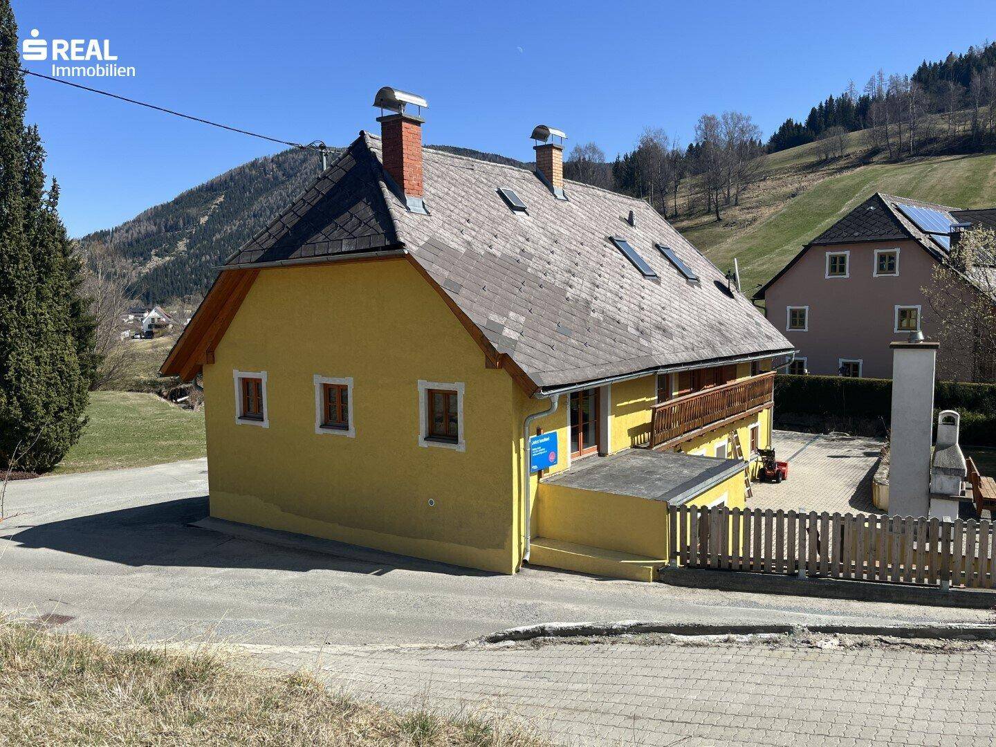 Rückansicht des gelben Hauses mit Holzbalkon, Dachfenstern und Schornsteinen.