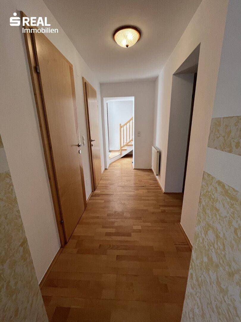 Heller Flur mit Holzparkettboden und Zugang zu mehreren Zimmern und einer Treppe.