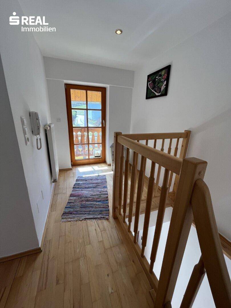 Oberer Flur mit Holztreppe, Teppichläufer und einer Tür mit Glasausschnitt zum Außenbereich.