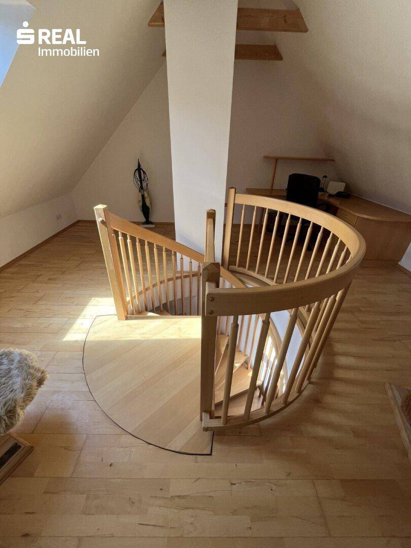Elegante Holzwendeltreppe führt vom Dachgeschoss in die darunterliegende Etage.