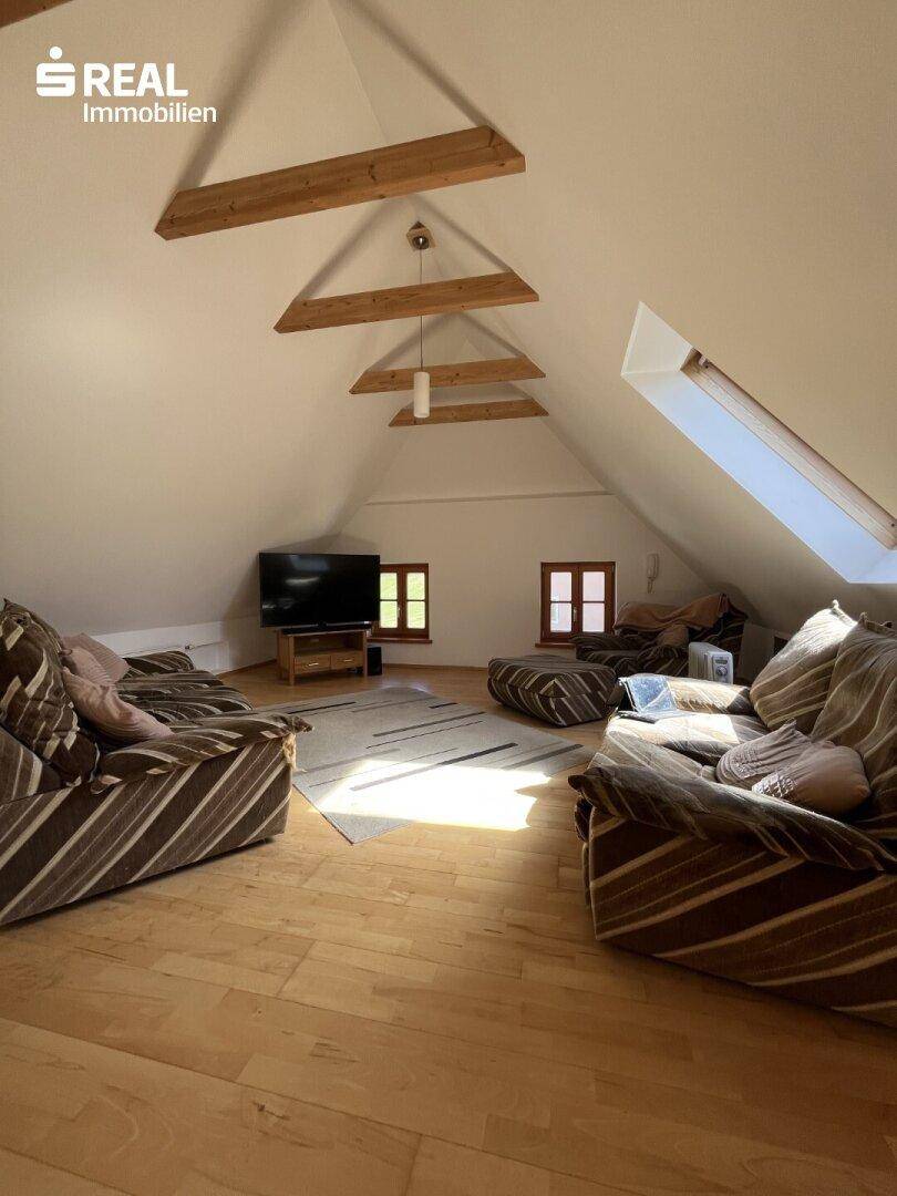 Dachgeschoss-Wohnzimmer mit bequemen Sofas, Holzboden und viel Tageslicht durch die Fenster.