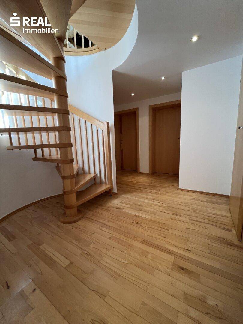 Heller Flur mit Holzwendeltreppe und Zugang zu weiteren Zimmern, ausgestattet mit Holzboden.
